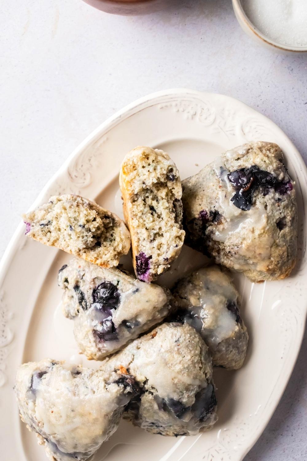 Part of a white plate with a couple of blueberry scones on it with one stone broken in half with the inside facing up.