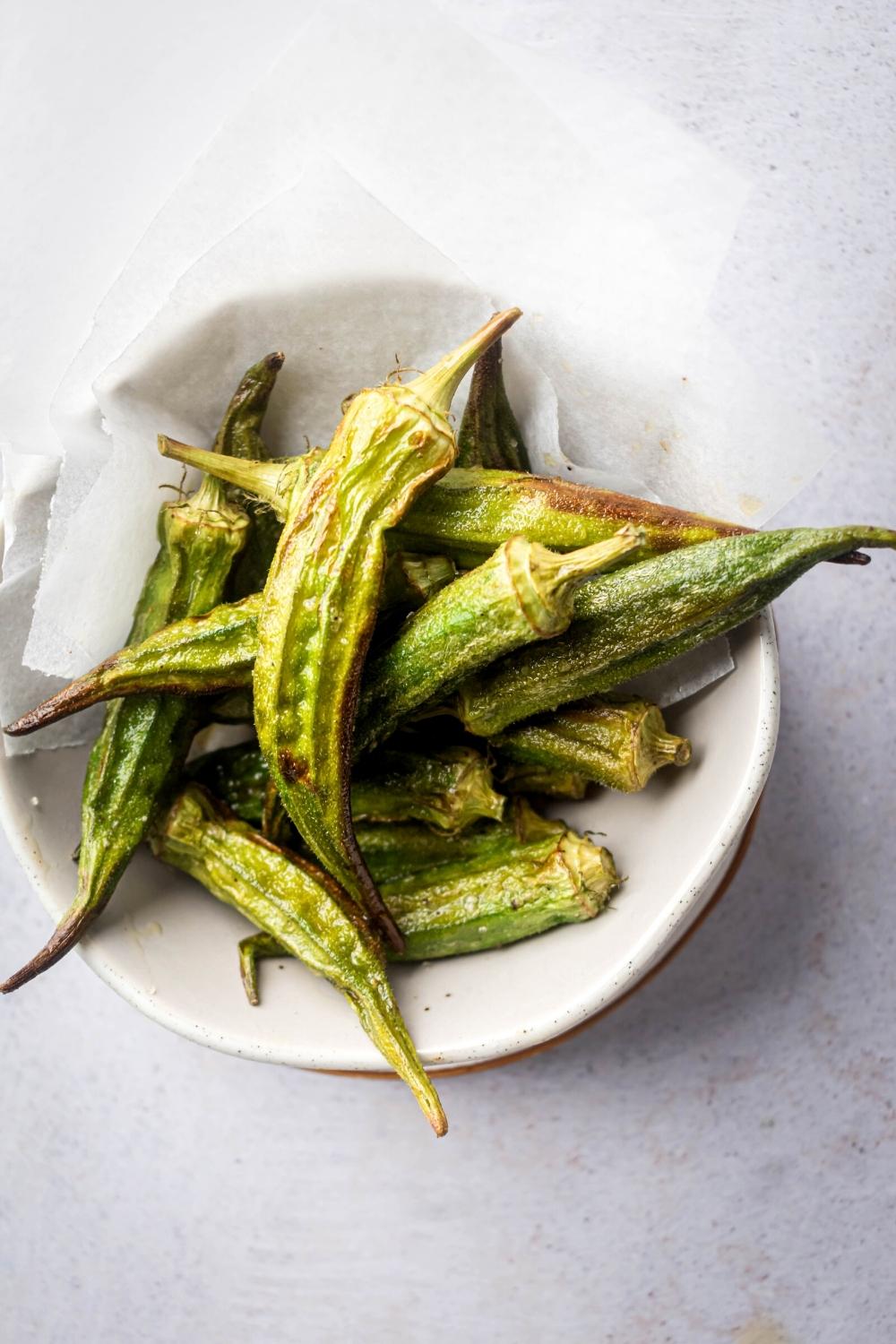 Fried okra on a sheet of parchment paper in a white bowl.