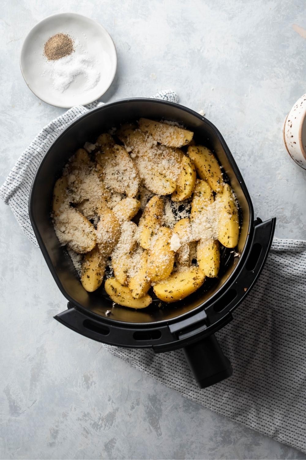 An air fryer filled with potato wedges with Parmesan cheese on top.