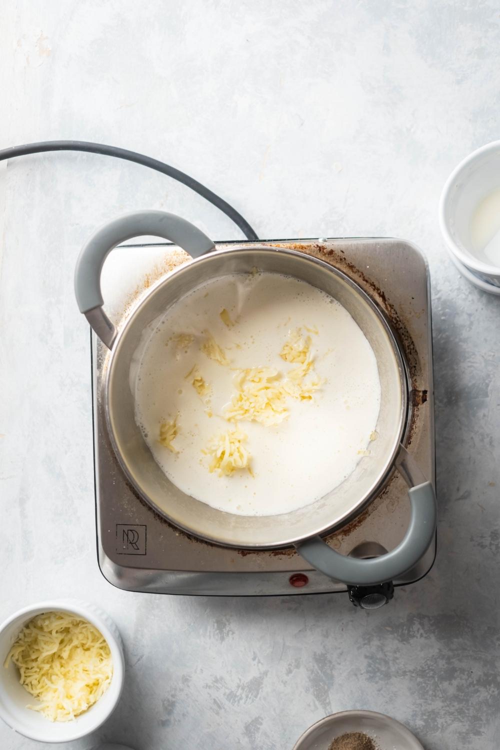 A pot on top of a burner on a white counter that is filled with heavy cream and shredded mozzarella cheese.