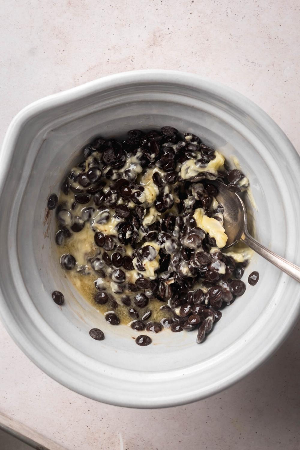 A white bowl filled with chocolate chips and butter mixed together with a spoon submerged in it.