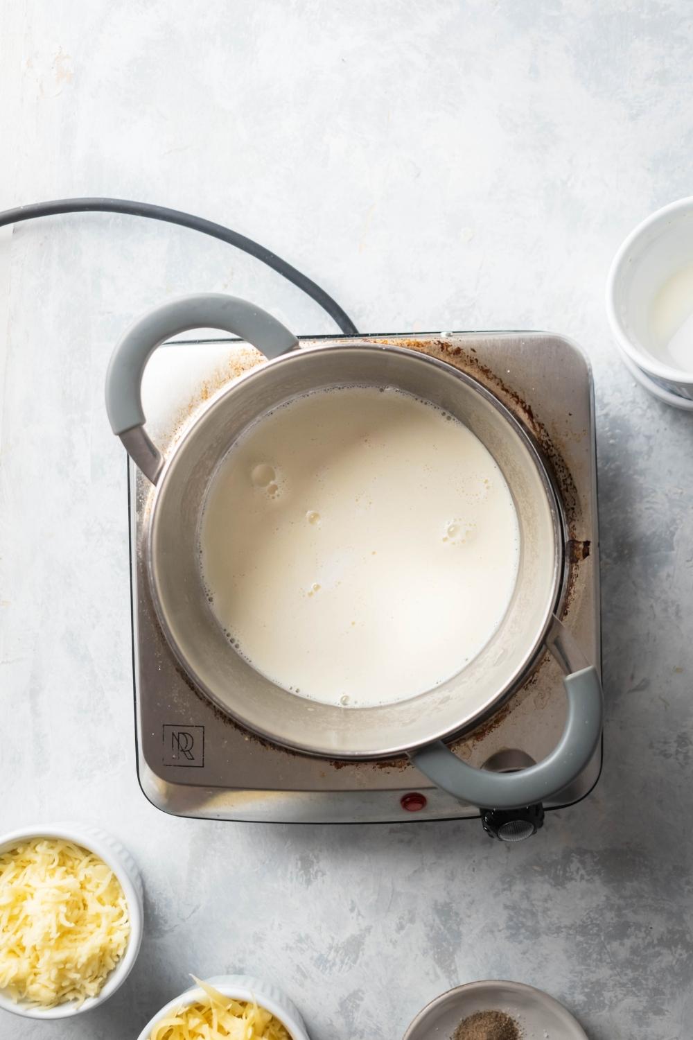 Cheese sauce in a pot on top of a burner on top of a grey counter.