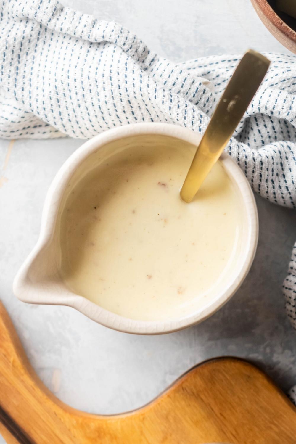 White queso and a white pitcher with a gold spoon submerged in it.