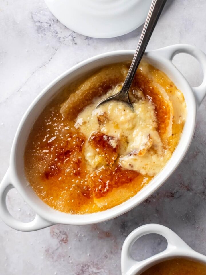 Crème brûlée and a large white ramekin with a spoon submerged in it.