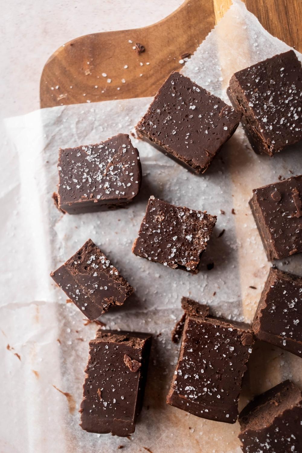 Two rows of three pieces of fudge on a piece of parchment paper on a wooden cutting board.