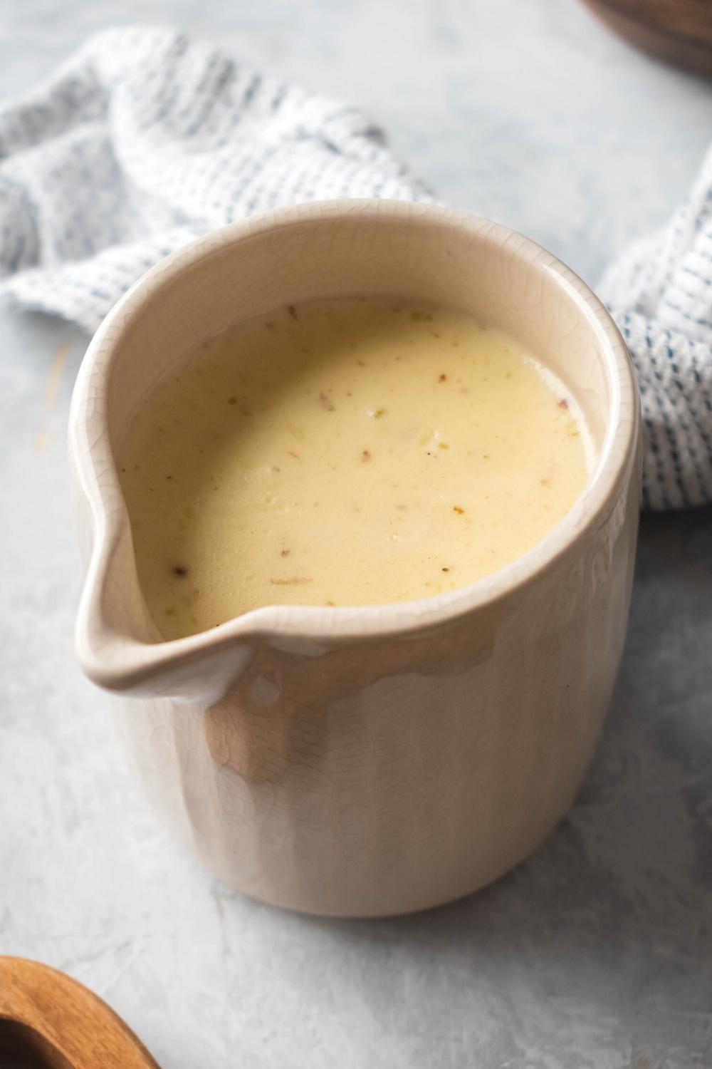 A white pitcher on a gray counter that is filled with white queso.