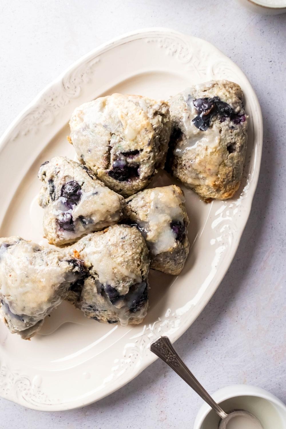 Six blueberry scones with glaze on top and a white plate.