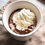 A white mug with hot chocolate in it with whipped cream on top.