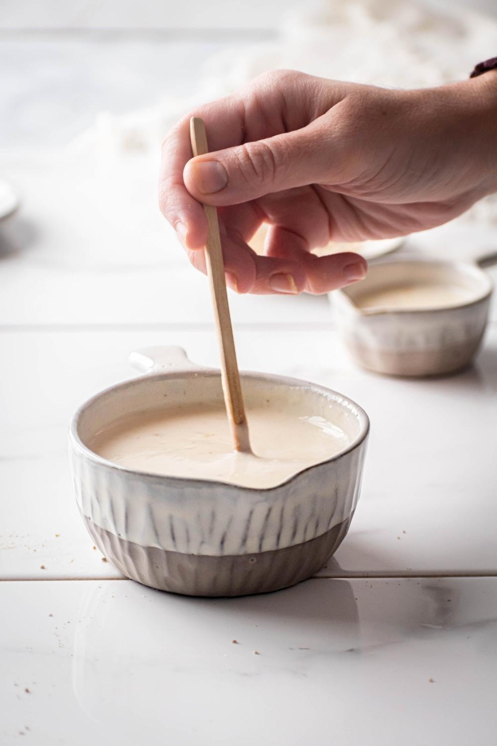 A hand holding a wooden spoon that is submerged in a bowl filled with keto white gravy.