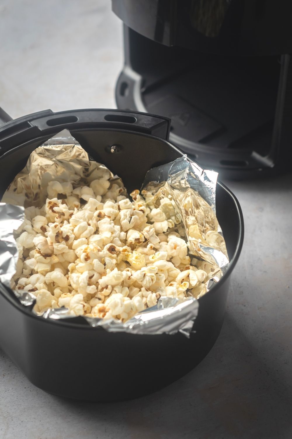 An air fryer basket lined with tin foil with popcorn in it.