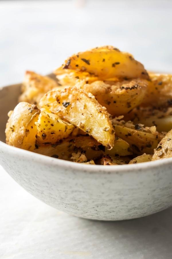 Part of a white bowl that is filled to the top with potato wedges.
