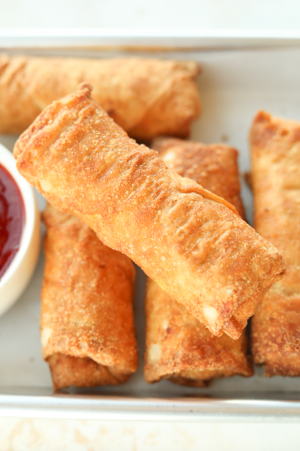 I eggroll diagonal across three other eggrolls on a piece of parchment paper on a baking sheet.