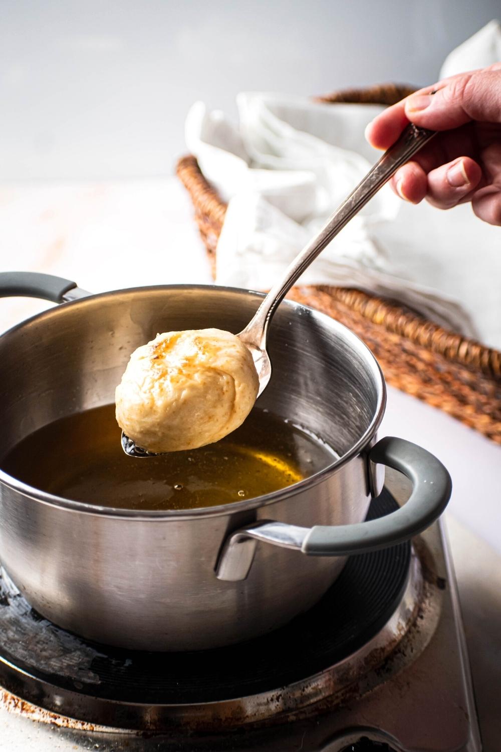A hand holding a spoon with a fried dumpling on top of it over a pot filled with oil.