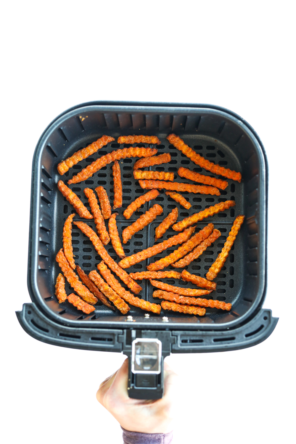Hand holding an air fryer with crispy sweet potato fries in the air fryer basket.
