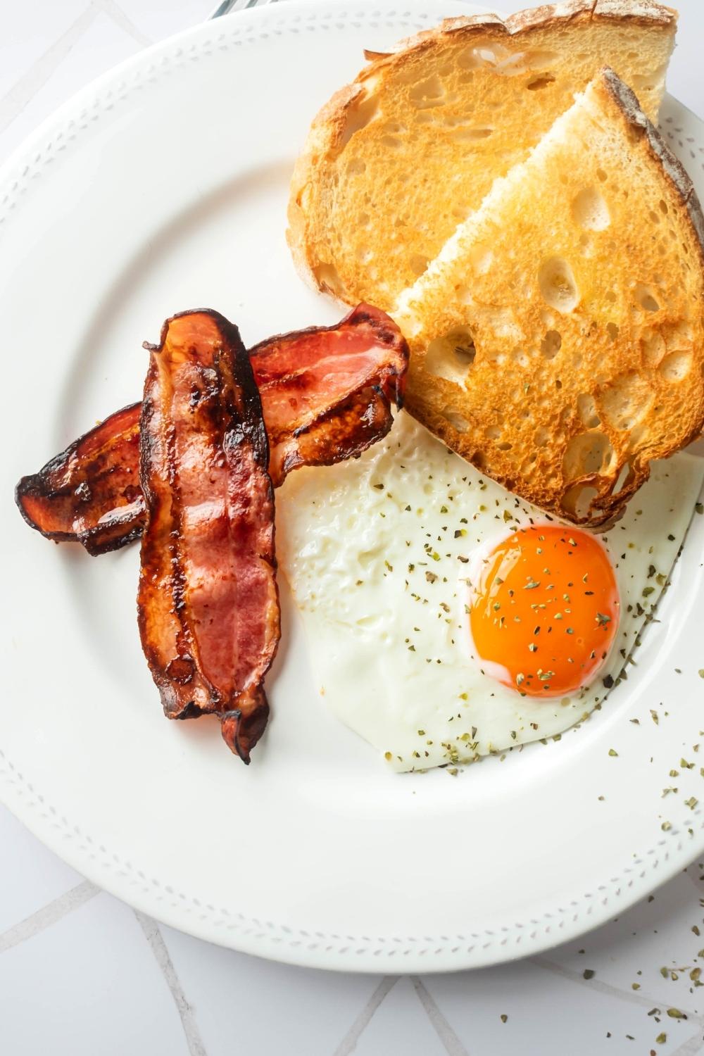 Two slices of turkey bacon, an egg, and toast on a white plate.