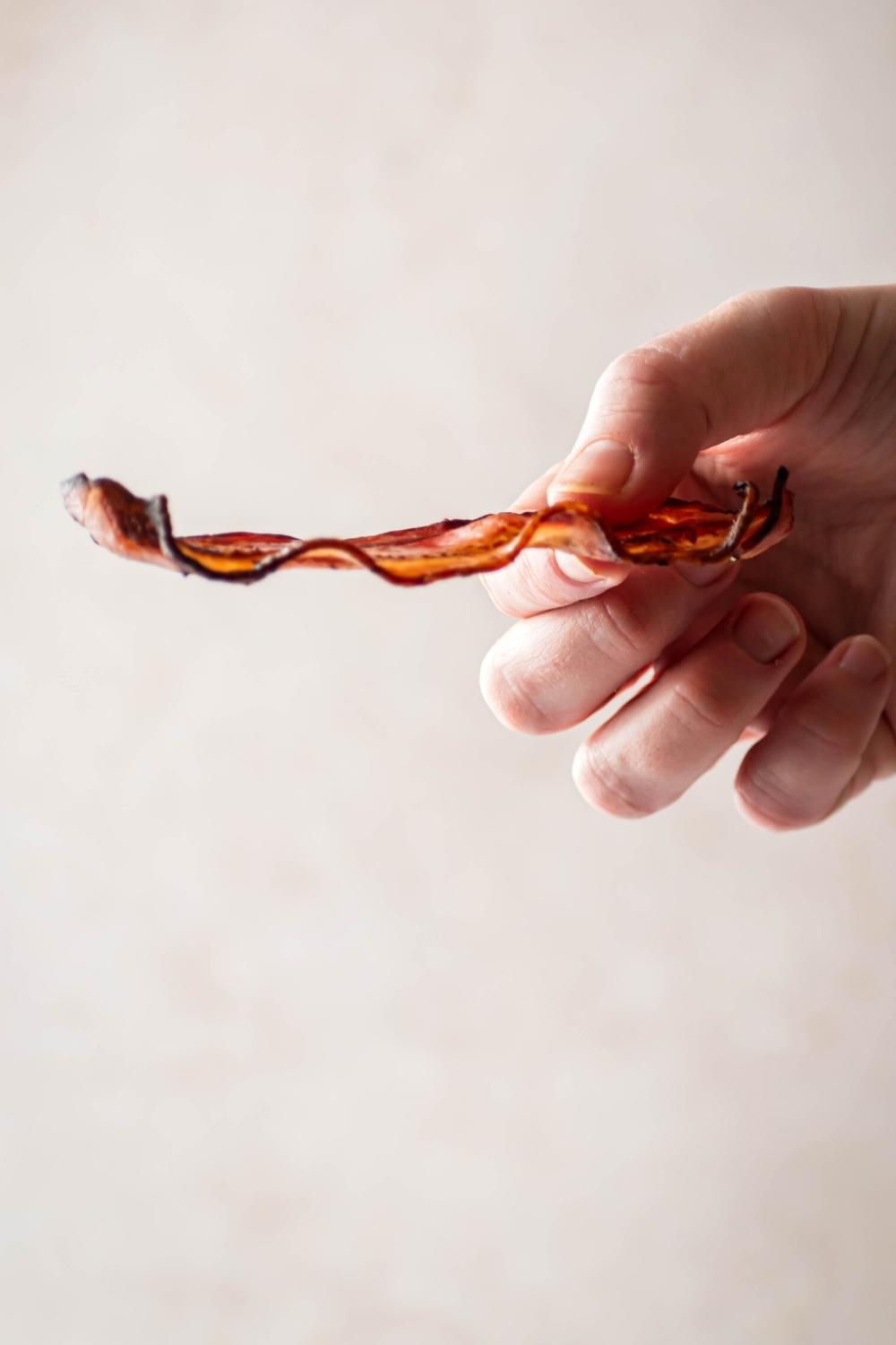 A hand holing a slice of turkey bacon horizontally.