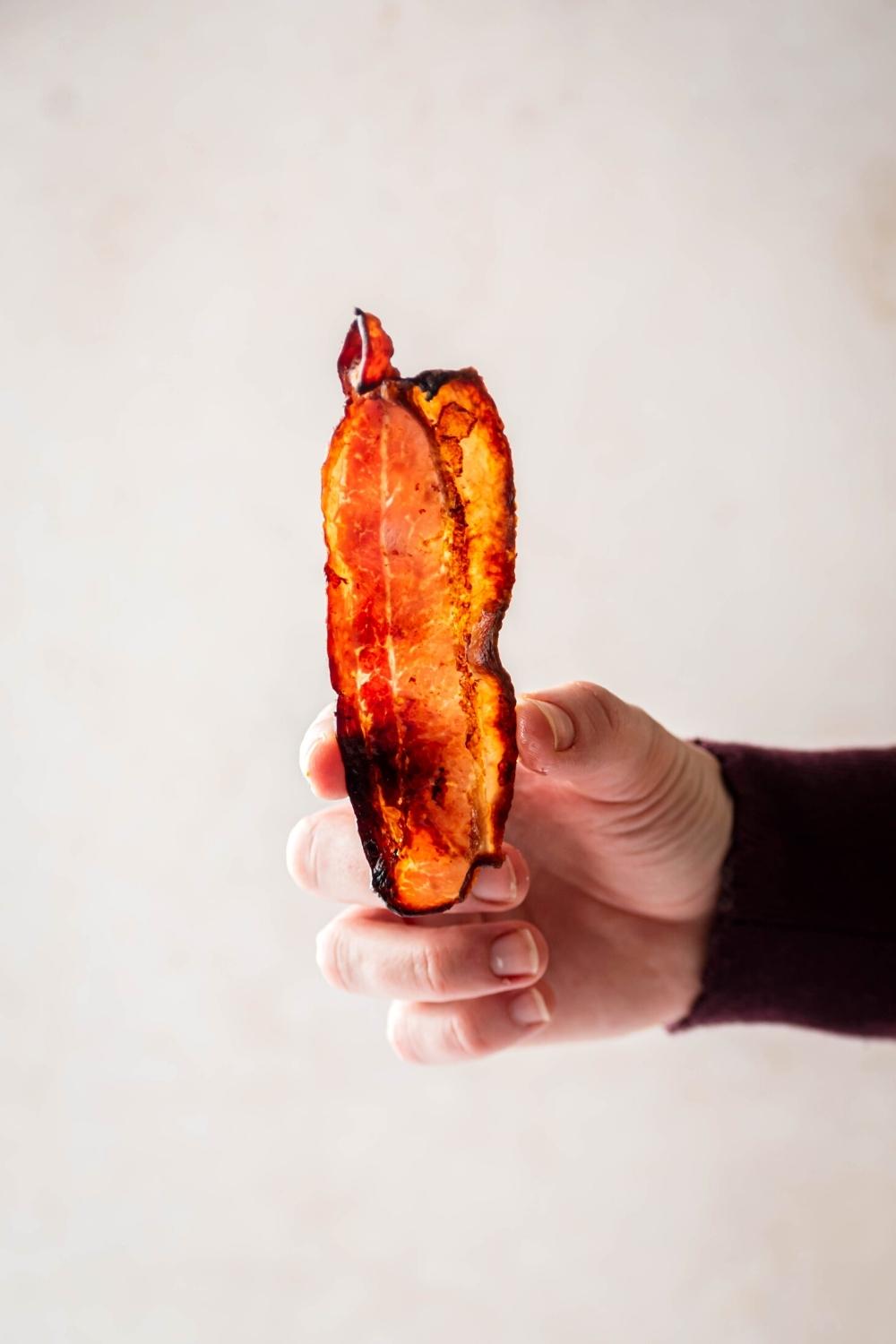 A hand holding a slice of turkey bacon vertically.