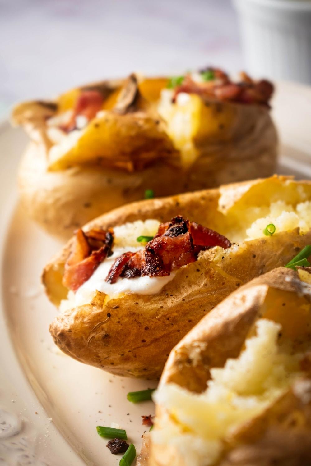 Part of three baked potatoes and part of a white plate.