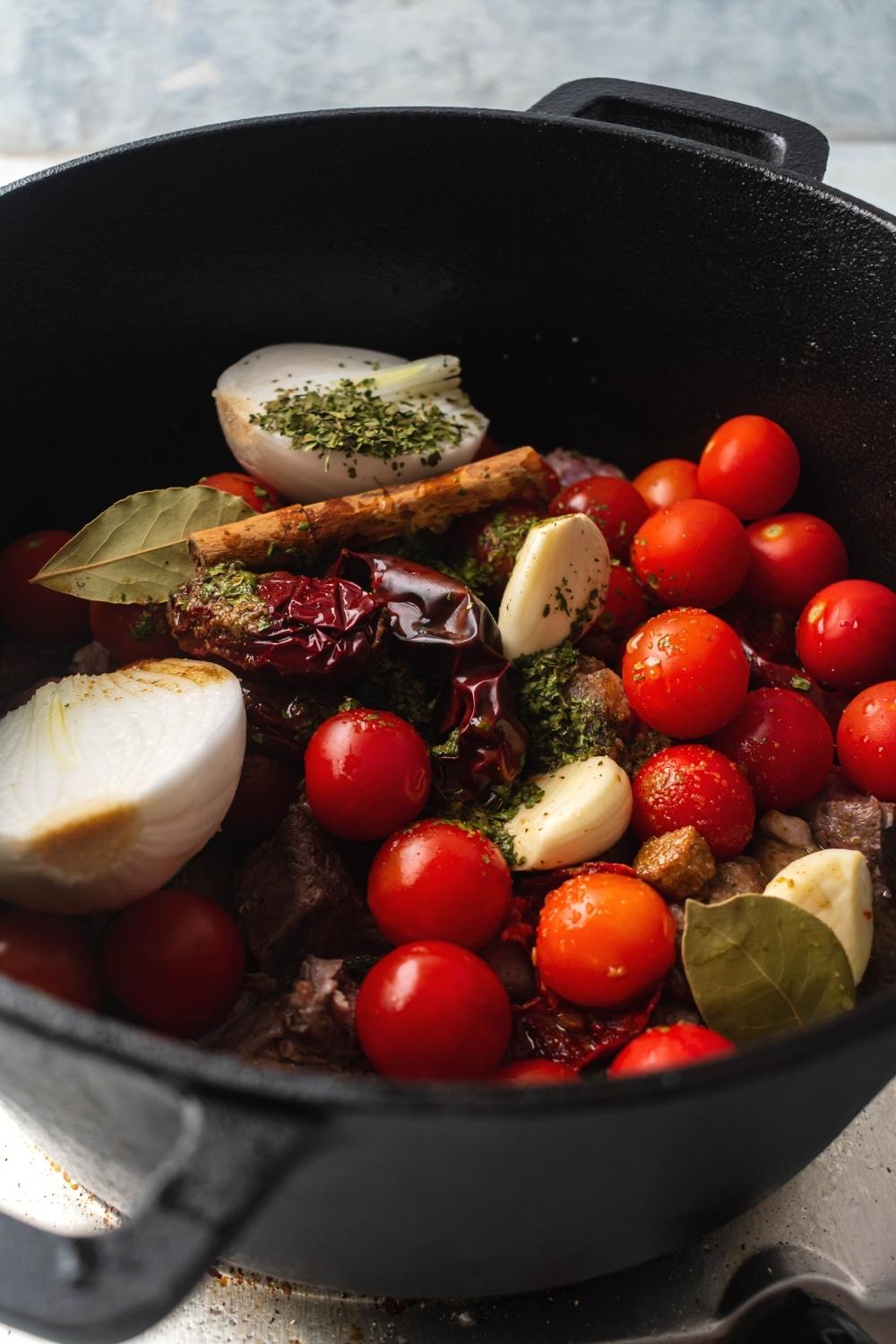 A Dutch oven filled with onion, tomatoes, chiles, and a bunch of spices and seasonings.