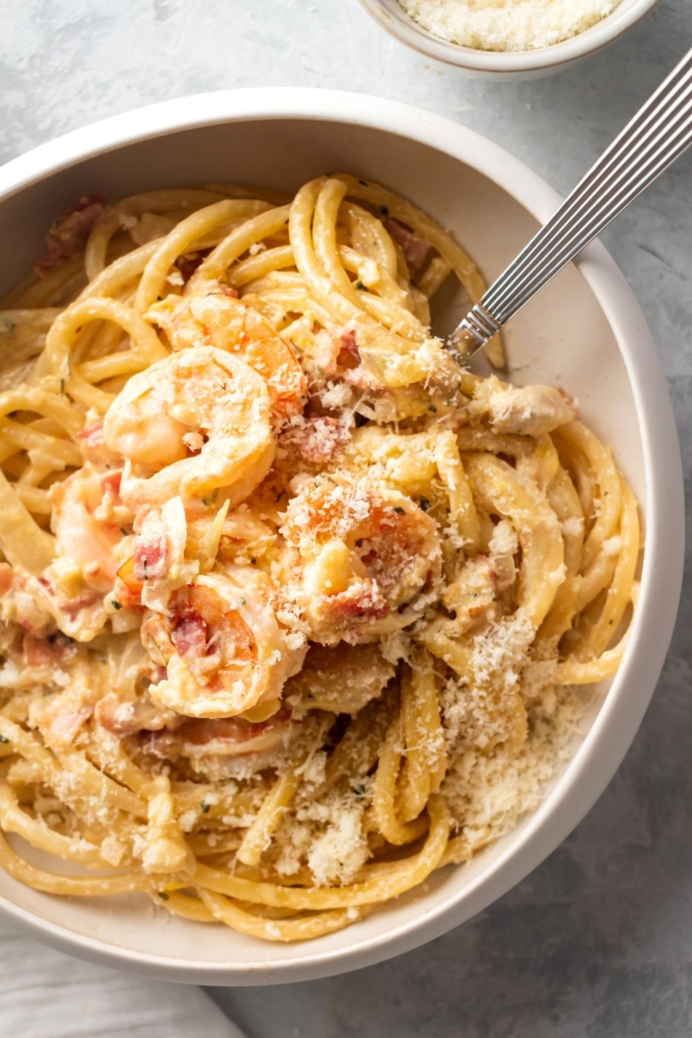 Chicken and shrimp carbonara and part of a white bowl with a utensil submerged in the pasta.