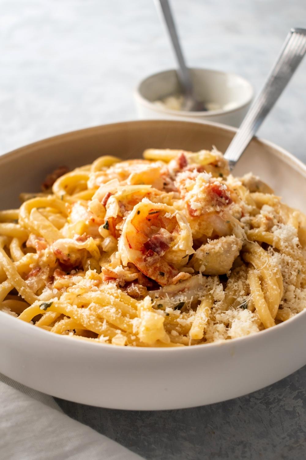 Part of a white bowl filled with chicken and shrimp carbonara.