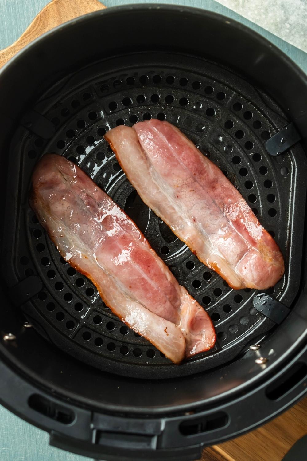 Two cooked slices of turkey bacon in an air fryer.