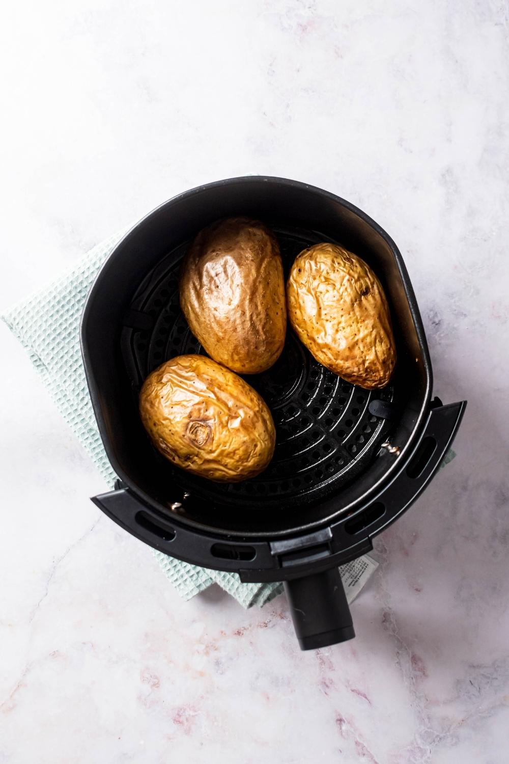 Three baked potatoes in an air fryer.