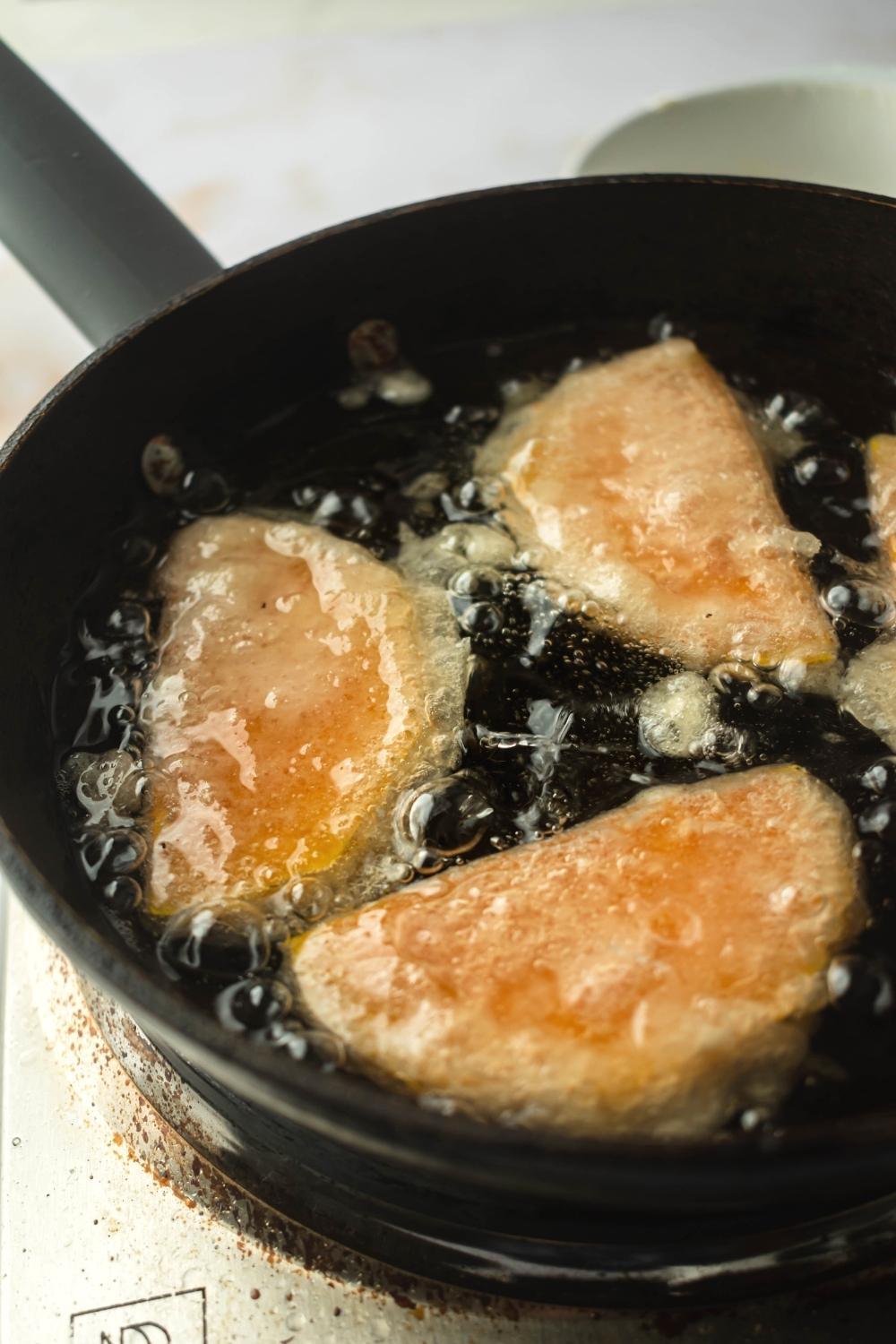 Part of a frying pan with three pieces of squash submerged in oil.