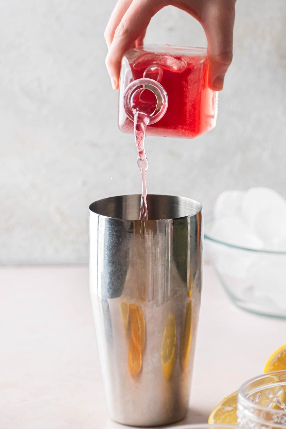 A hand pouring pink lemonade into a stainless steel mixing cup.