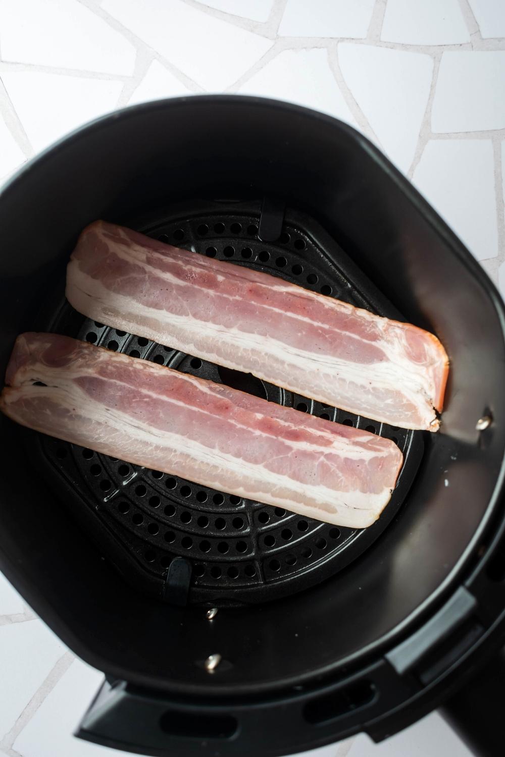 Two uncooked slices of turkey bacon in an air fryer.
