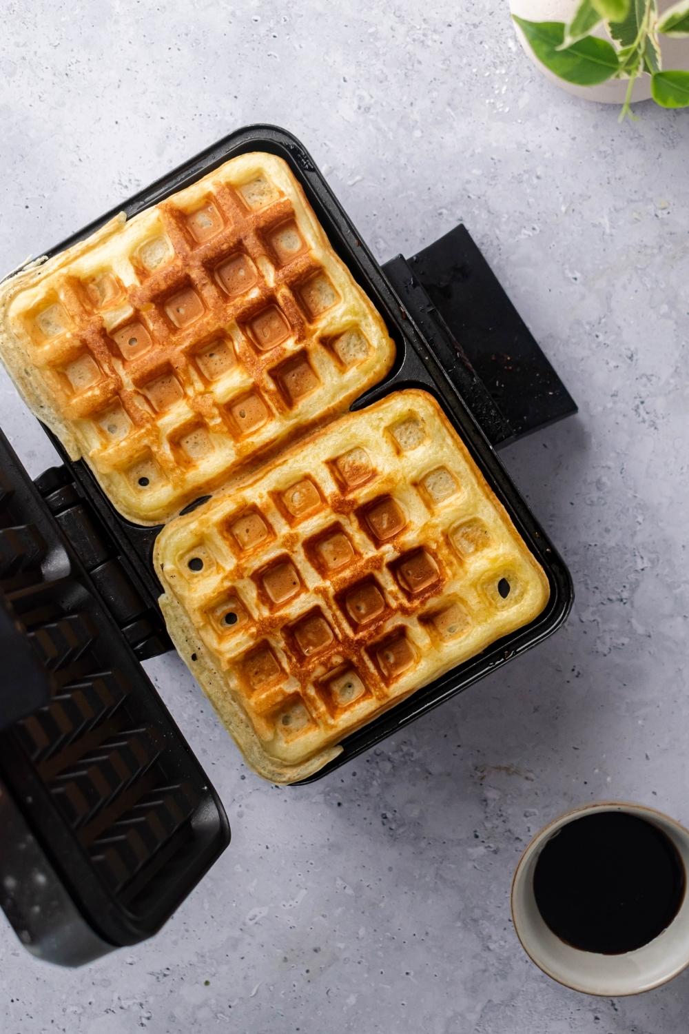 And opened waffle iron with two cooked waffles in it.