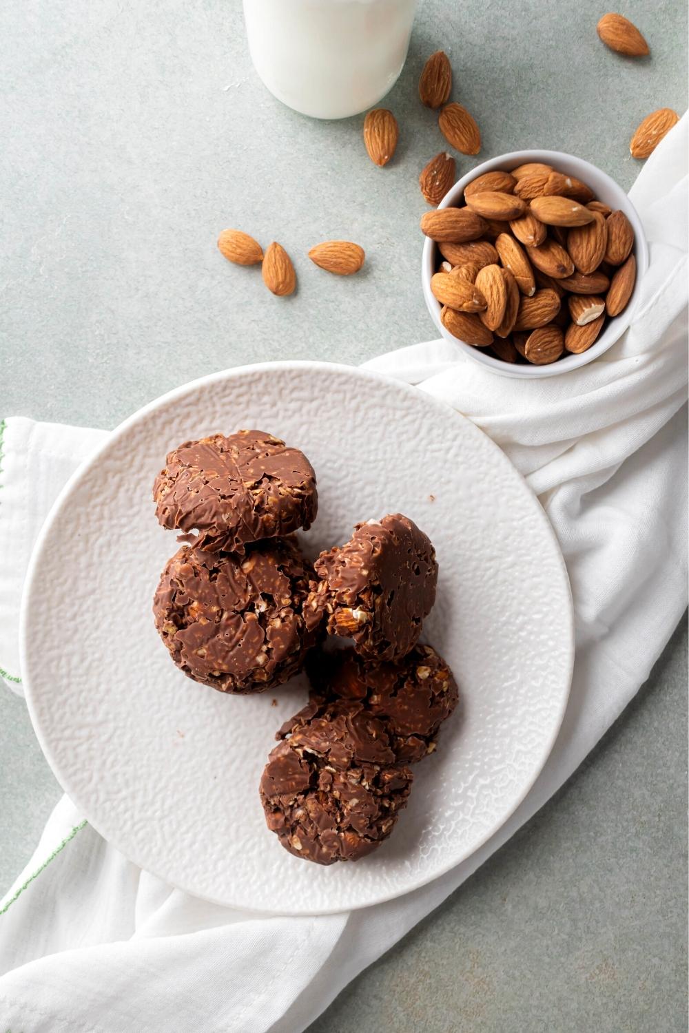 No bake cookies on a white plate on a white tablecloth on top a grey counter, Behind the plate is a bowl of almonds.