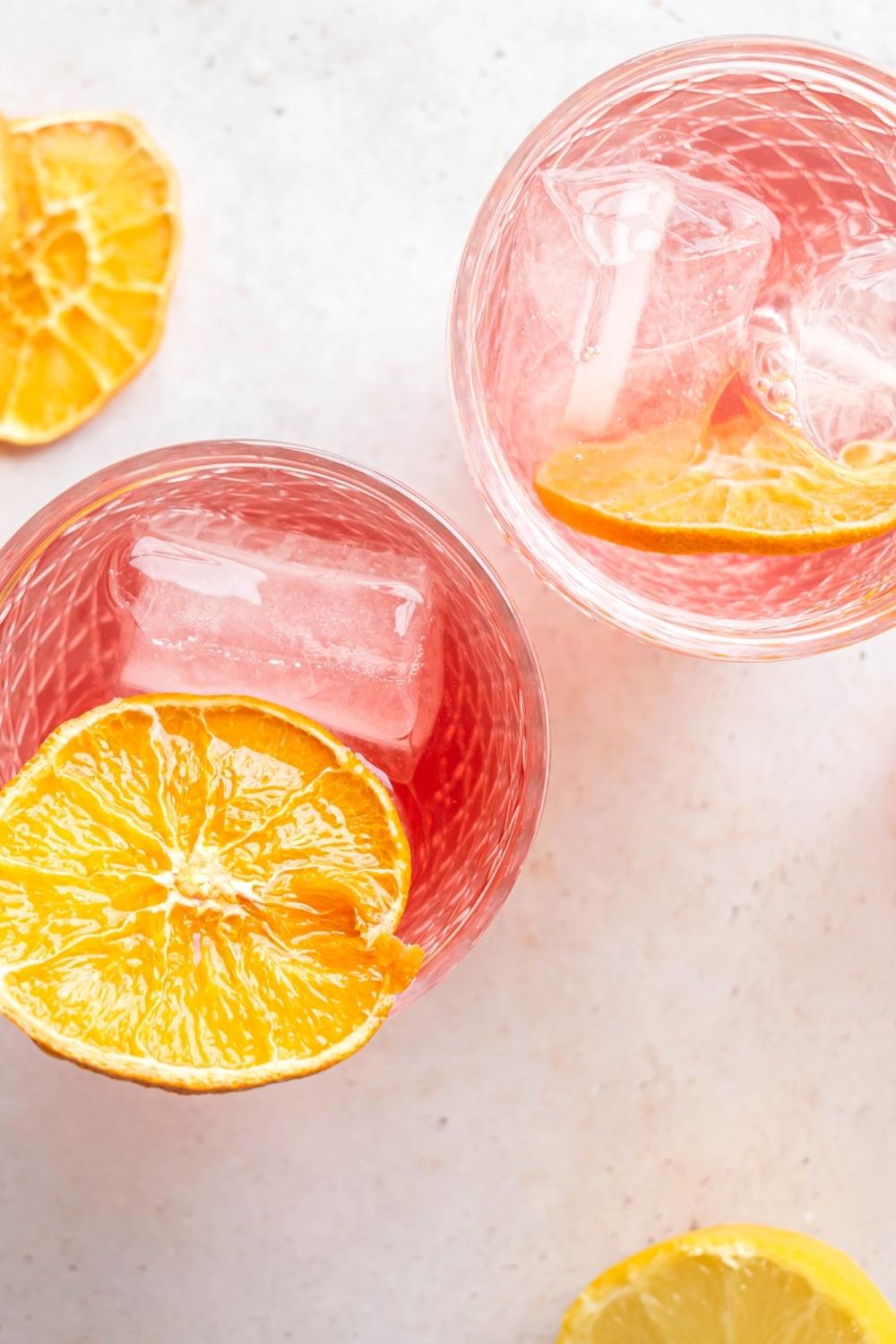 Two glasses on a white counter. The glasses are filled with a lemon slice, ice cubes, and pink lemonade vodka.