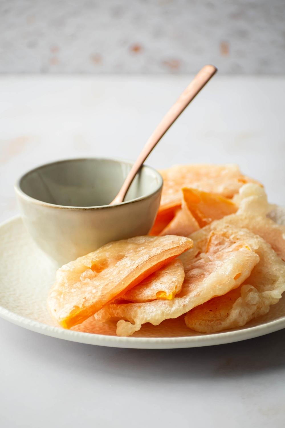 A bunch of pieces of fried squash on a white plate with a bowl and a wooden spoon in it.