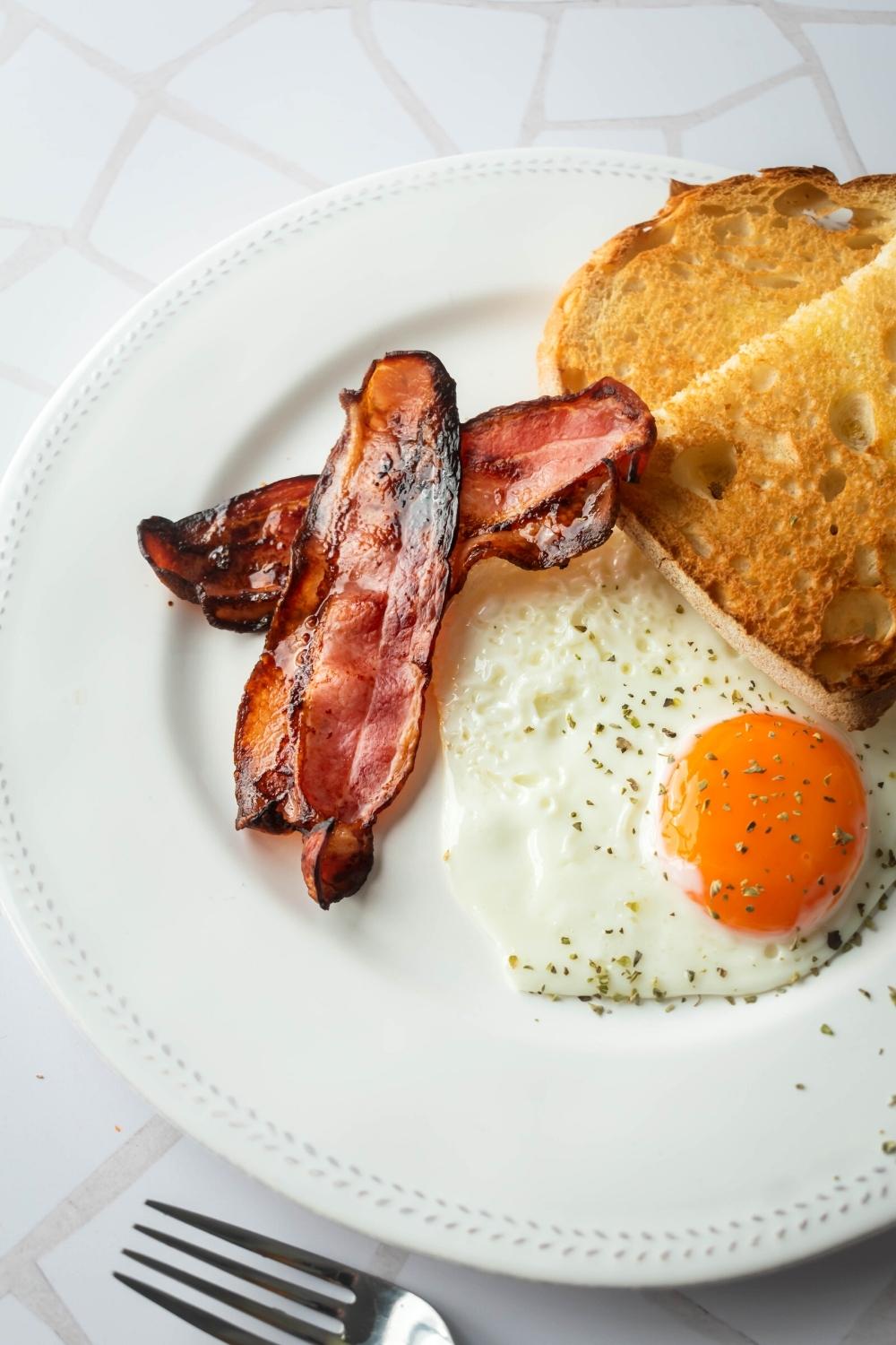 Part of a white plate with part of two slices of toast, an egg, and two slices of turkey bacon.