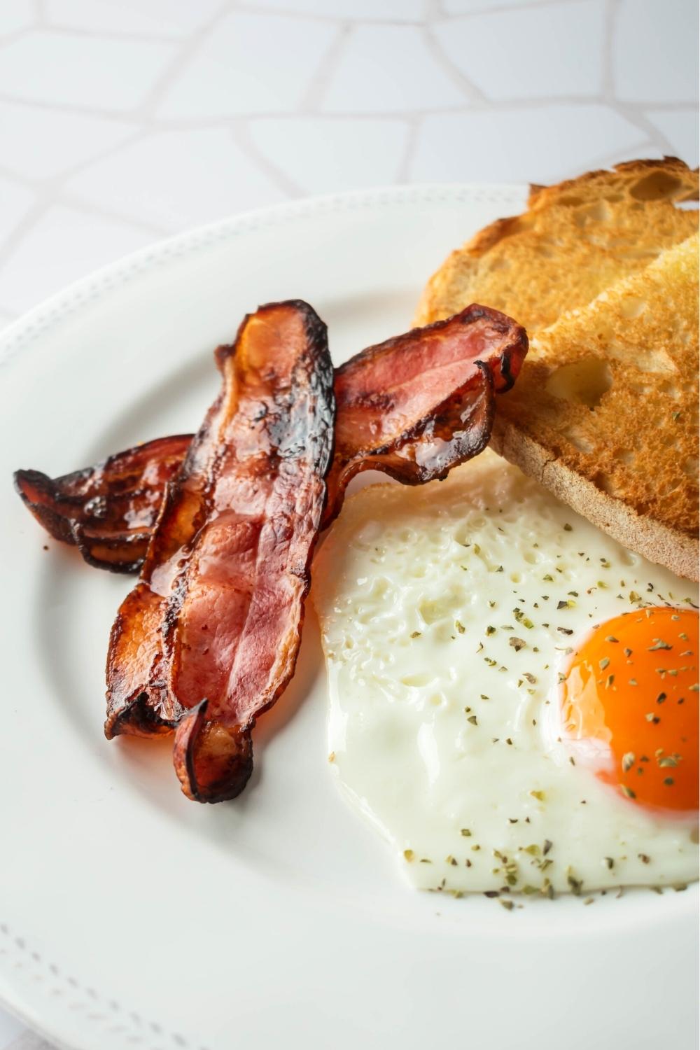 Part of a white plate with part of toast, part of an egg, and two slices of turkey bacon.