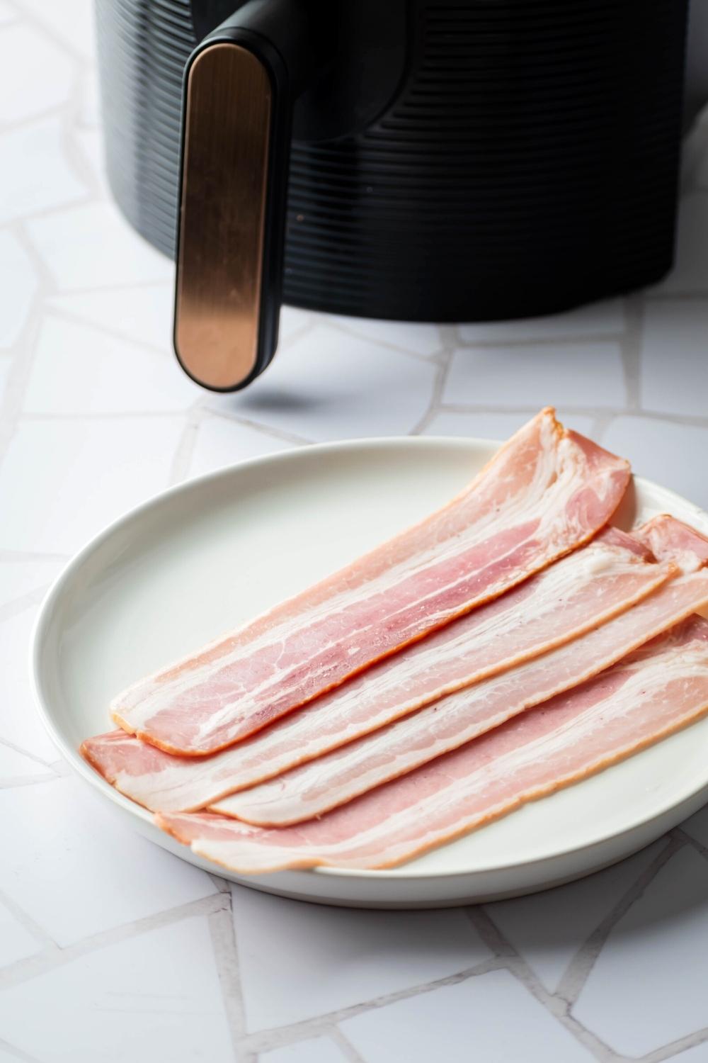 A white plate with four uncooked slices of turkey bacon on it.