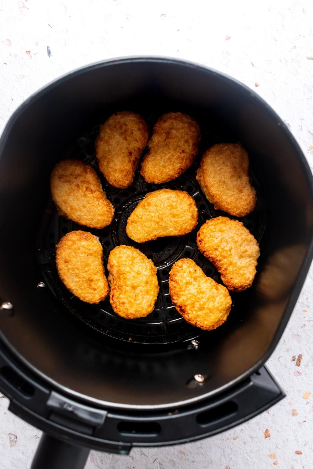 Eight chicken nuggets lying flat in an air fryer.