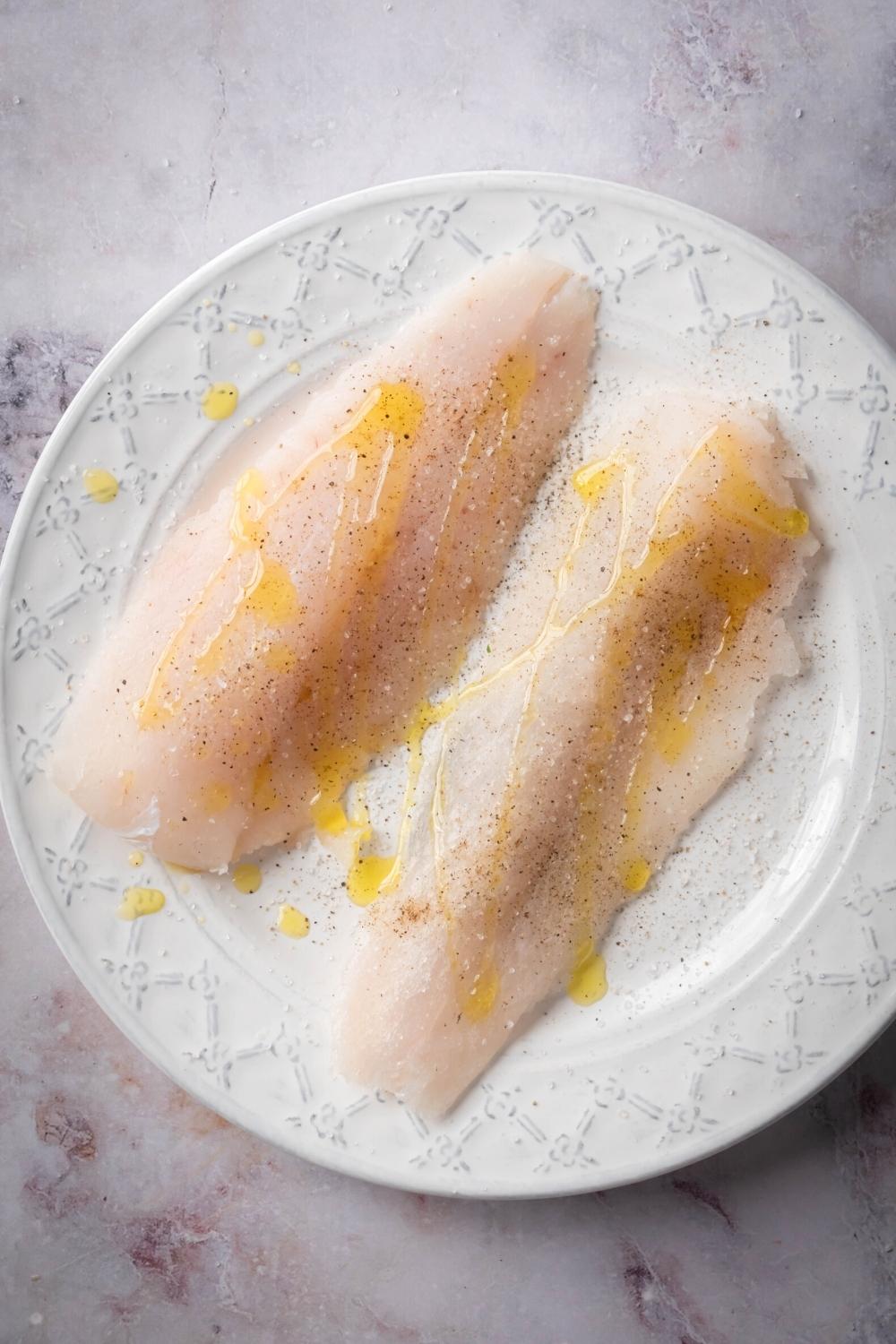 Two raw mahi mahi fillets with olive oil drizzled on them on a white plate.