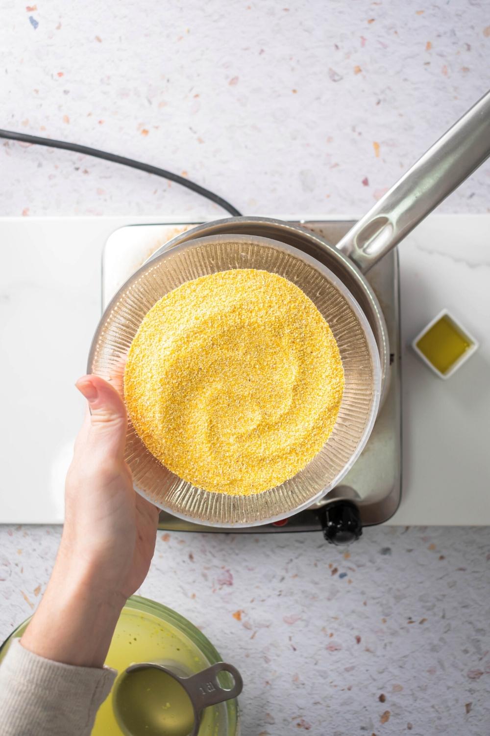 A hand holding a glass plate that is filled with polenta flour.