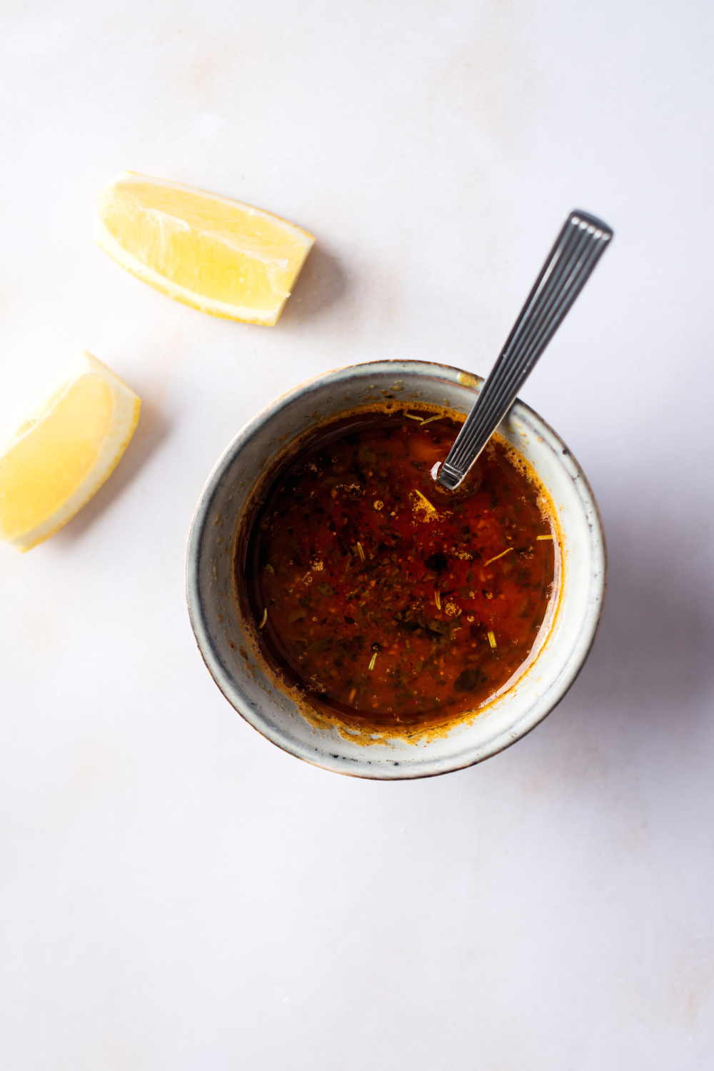 Are utensil in a cup of beloved sauce that is on a gray counter. Behind it or two lemon wedges.