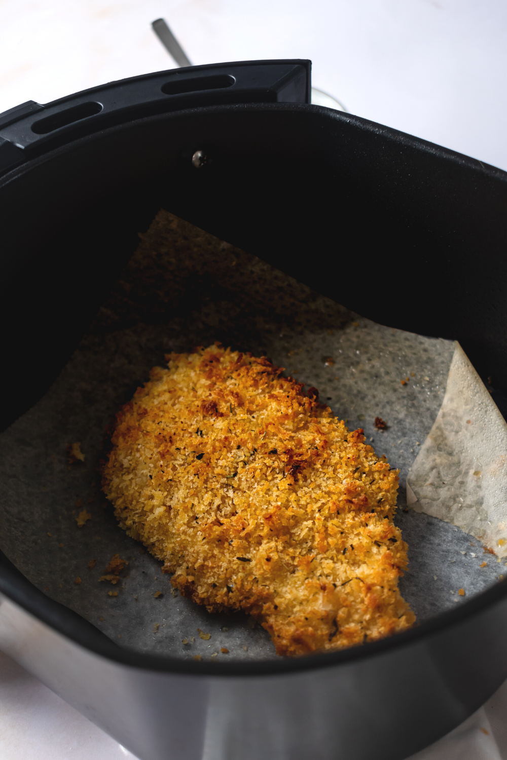A piece of breaded fried catfish on a paper towel in an air fryer.