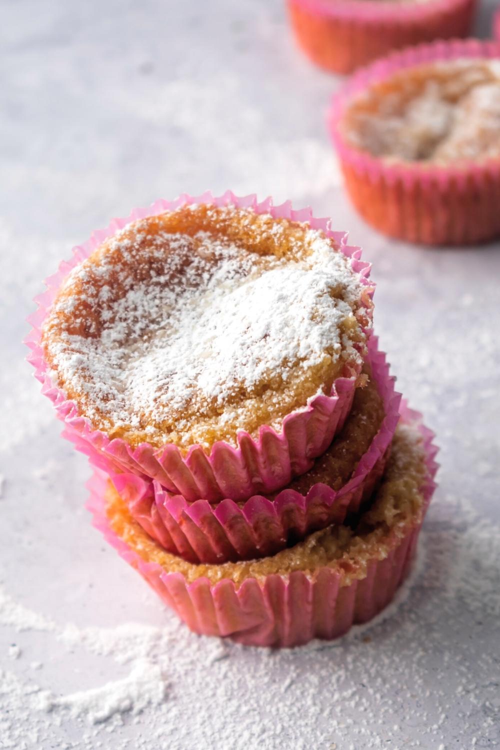 A stack of three mochi muffins with powdered sugar on the top one.