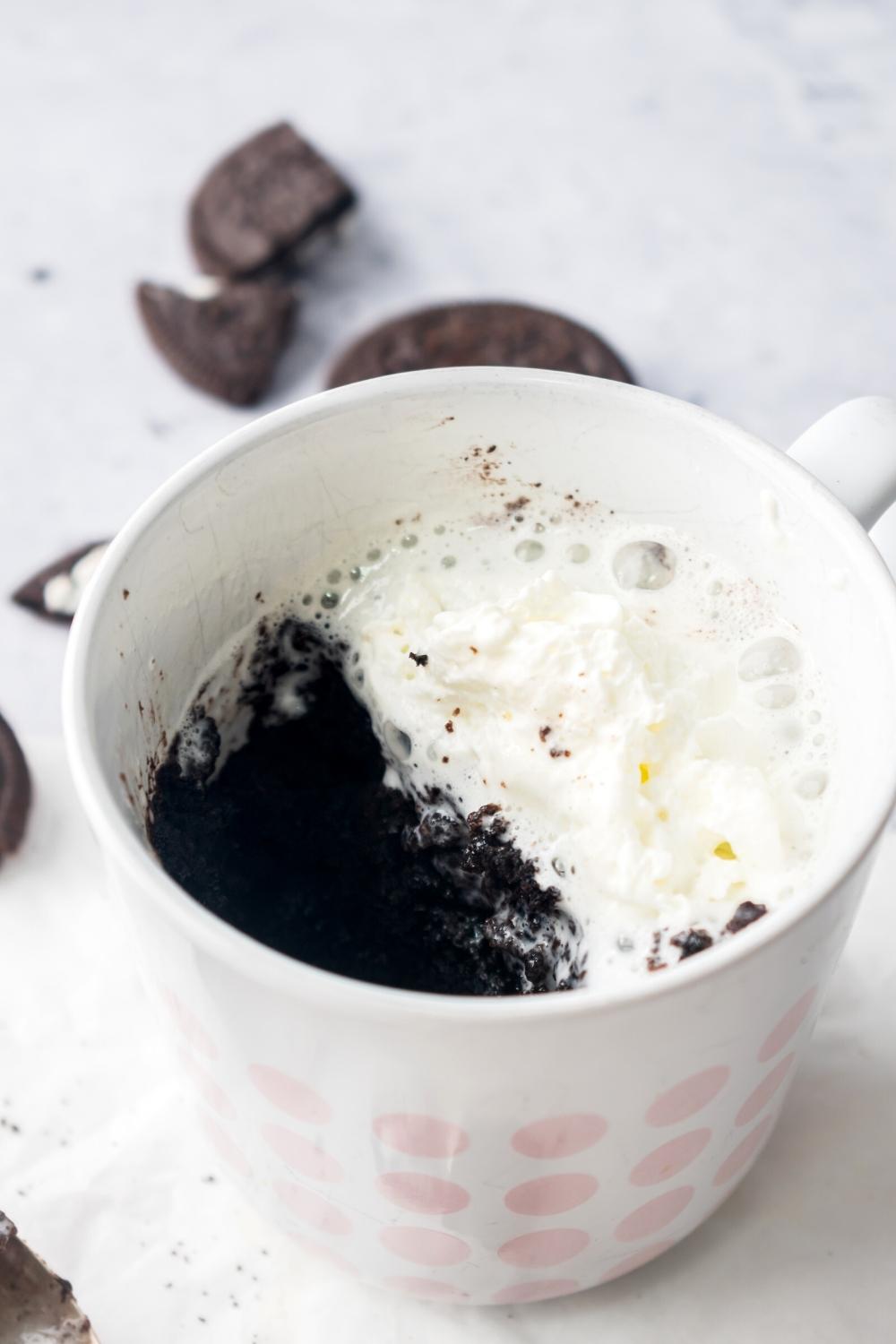 A mug filled with an Oreo mug cake with half of the cake showing and the other half covered in whipped cream..
