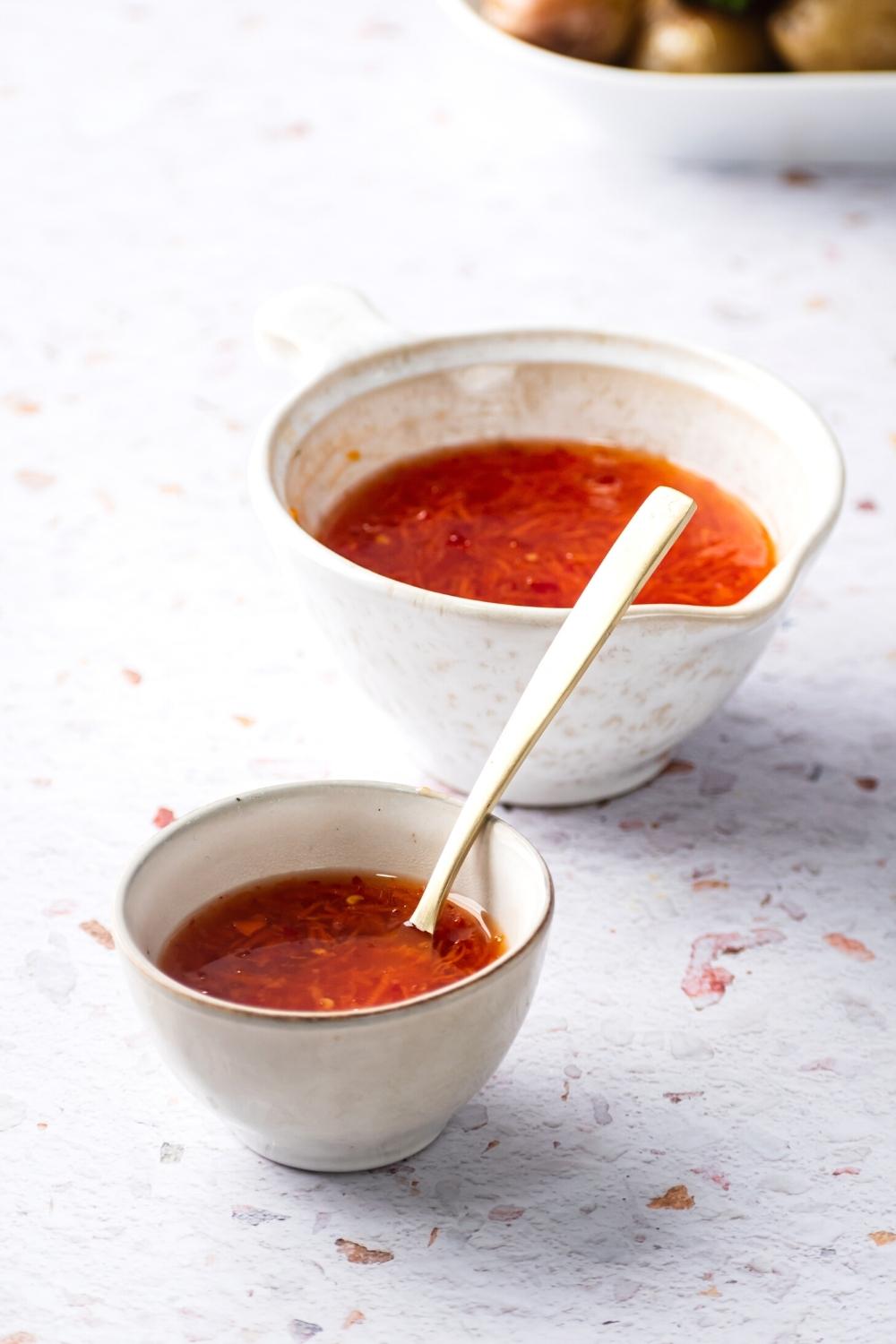 Sweet chili sauce in a small white cup and a medium white cup on a white counter.