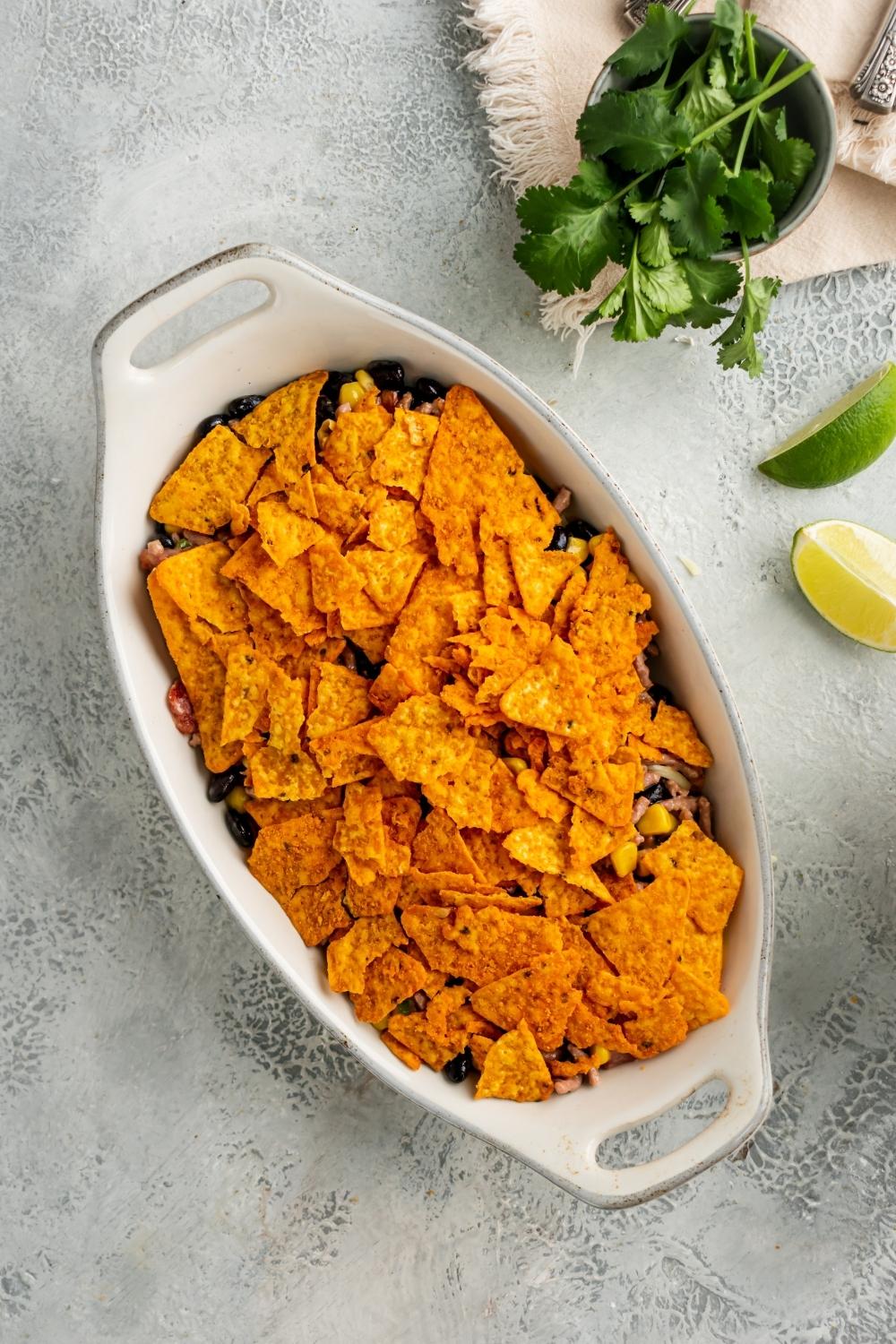 Crushed nacho cheese flavored Doritos on top of the Doritos casserole in the white casserole dish.