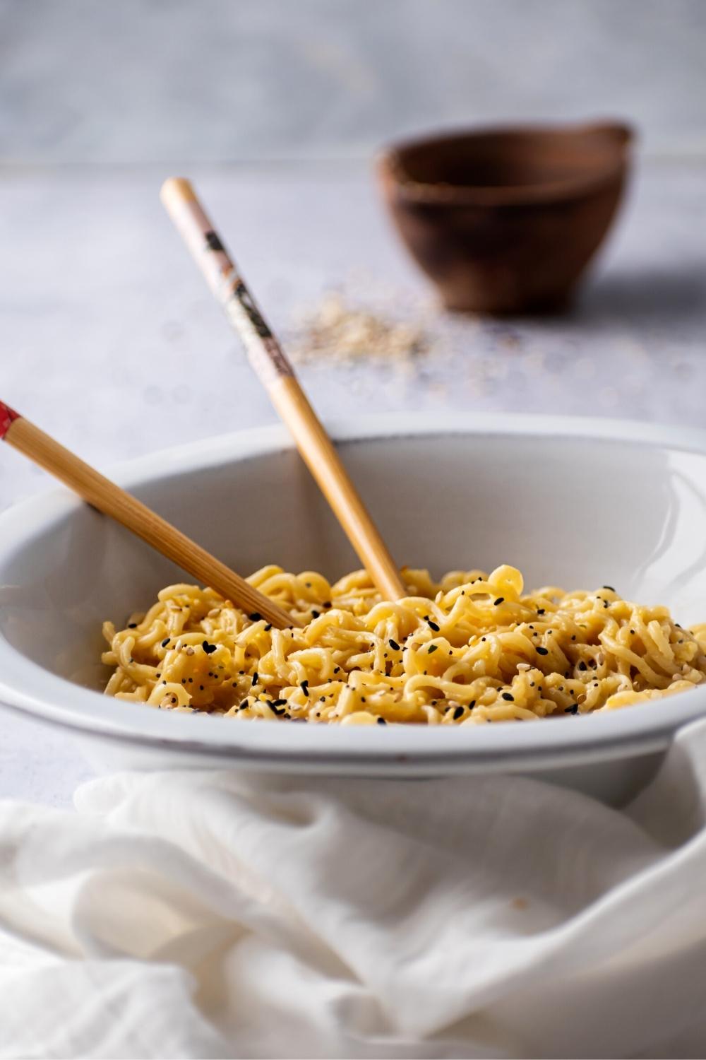 Uber part of a white bowl filled with Ramen noodles with one chopstick and part of another chopstick in the noodles.