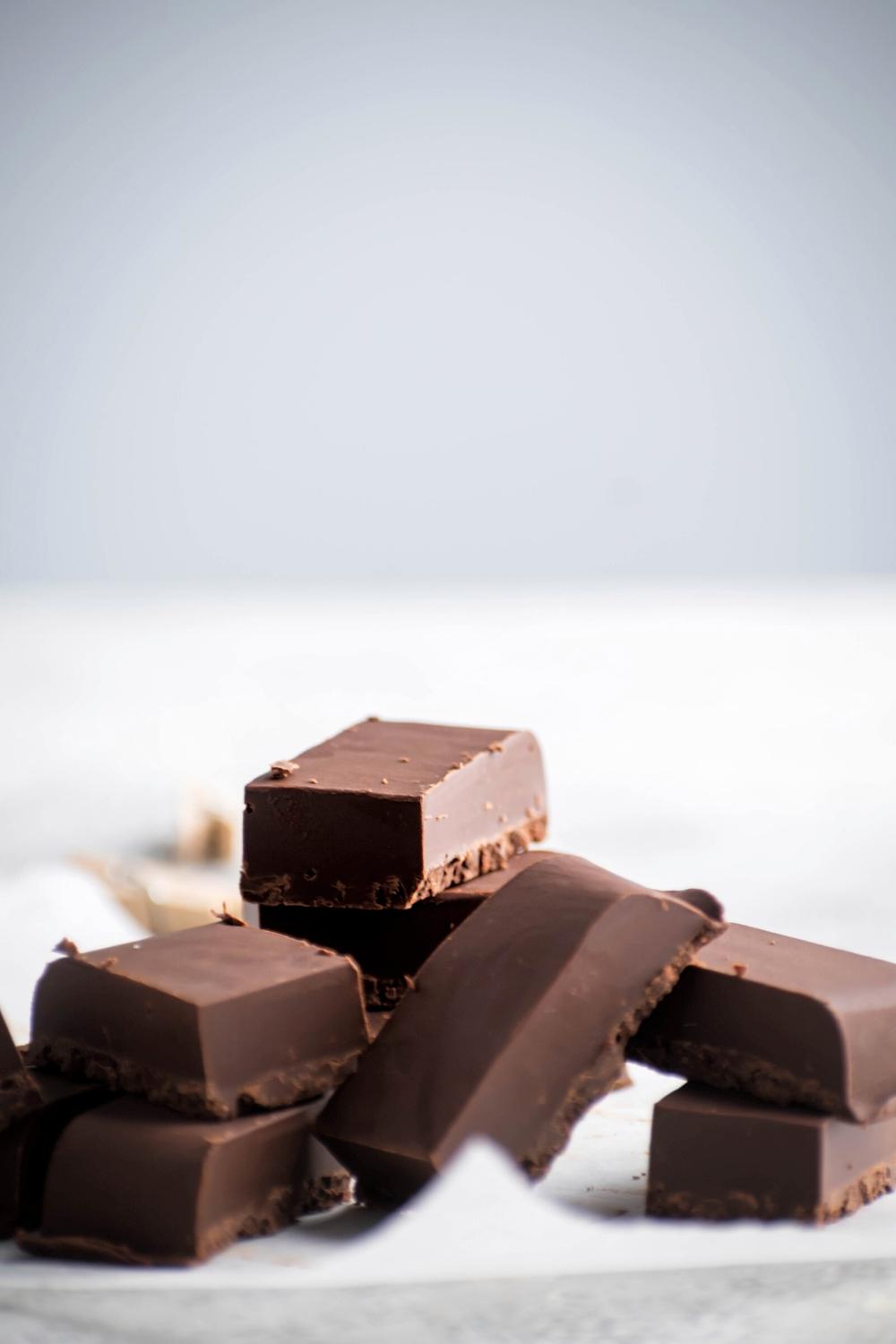 A few pieces of 2 ingredient fudge stacked on each other on a sheet of parchment paper.