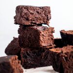 A stack of three brownies with a few brownies surrounding them on a piece of parchment paper.