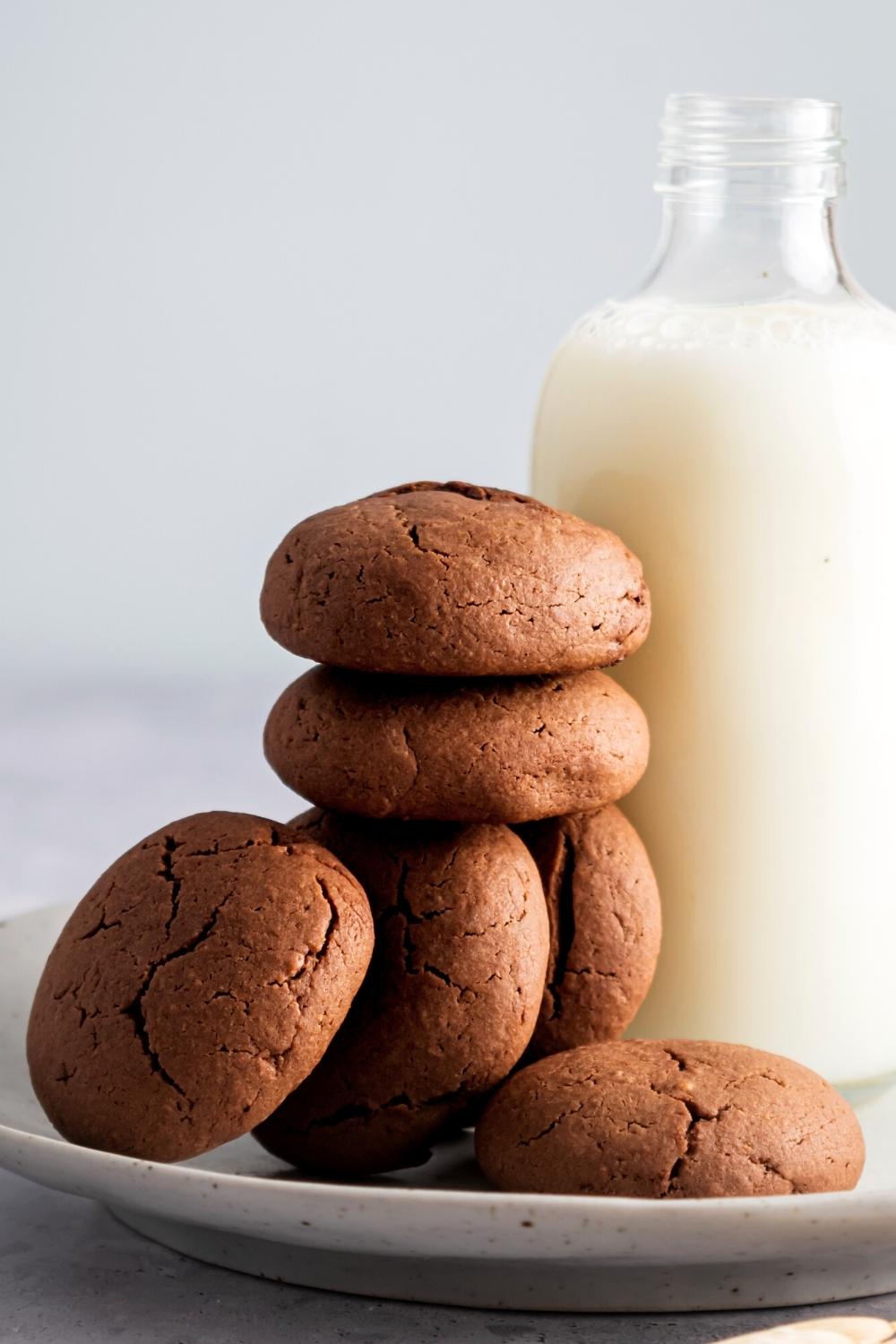 A Nutella cookie on a plate, three Nutella cookies standing up vertically on the plate, two Nutella cookies stacked on top of those, and part of a glass jar of milk next to the cookies.